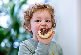 Ein kleiner Junge beißt in ein Brötchen mit Schokoladencreme