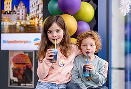 Ein Mädchen und ein Junge sitzen nebeneinander und trinken mit Strohhalme auf Bechern mit blauen Slush-Eis. 