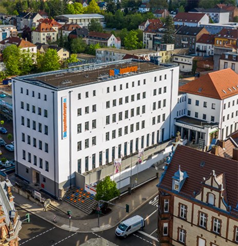 Außenansicht der Jugendherberge Pirmasens. Ein großes weißes Gebäude in der Stadt mit blau-orangen Logo auf dem Dach.