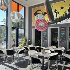 Bistro der Jugendherberge Trier mit weiß-schwarzen Stühlen und Tischen. Links ist eine große Fensterfont. Von der Decke hängen große rosa Ballons in Form eins Donuts. 