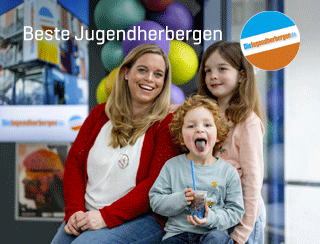 Beste Jugendherbergen. Eine fröhliche Familie, bestehend auf Mutter, Tochter und Sohn, in der Jugendherberge Trier. Die Mutter lacht, die Tochter lächelt und der Sohn hält einen Becher mit blauem Slush-Eis in der Hand und streckt die blaugefärbte Zuge raus. 