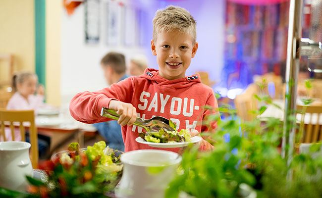 Glücklicher Junge am Salatbüfett im Restaurant der Jugendherberge.